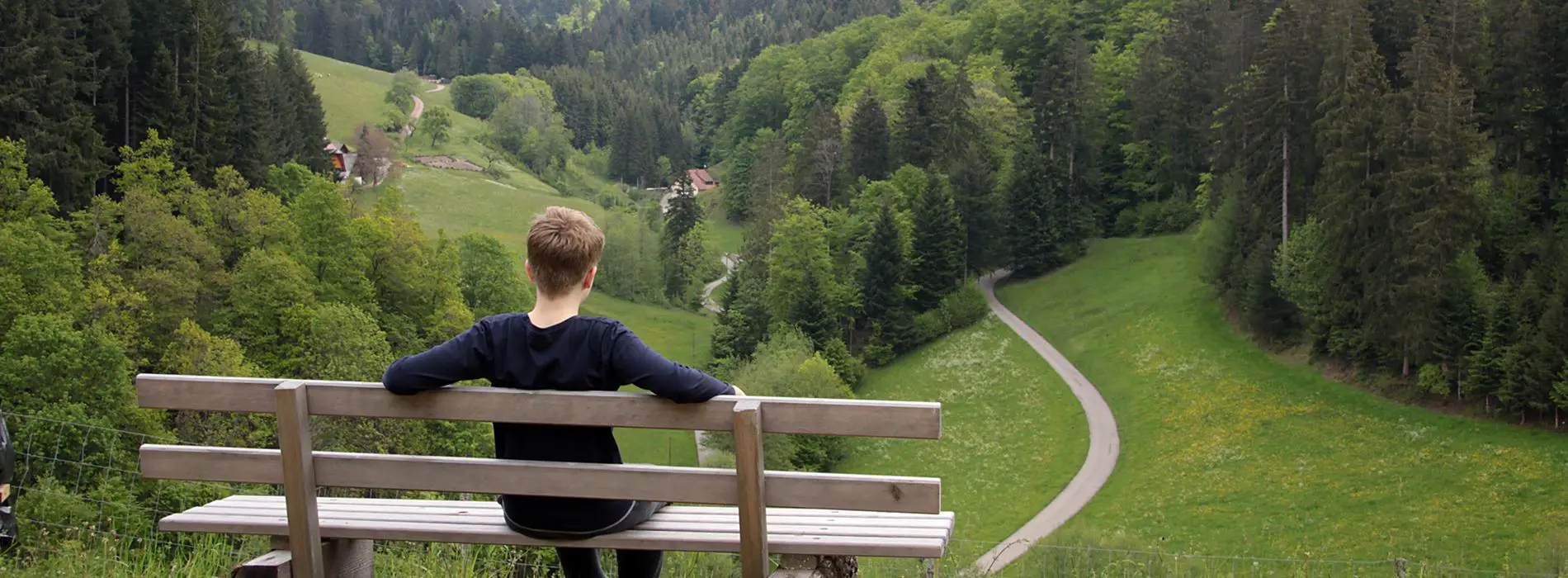 Junge auf einer Sitzbank mit Blick ins hintere Zuwälder Tal